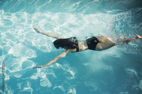 Woman in bikini swimming underwater in sunny swimming pool