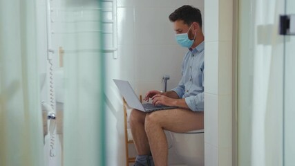 Close up businessman working on laptop wearing mask sit on the toilet at home restroom bearded funny wc isolation quarantine pandemic coronavirus covid-19 portrait close up slow motion