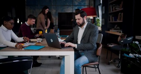 Wall Mural - Zoom in portrait of happy young bearded Caucasian businessman smiling at camera using laptop at loft office workplace.