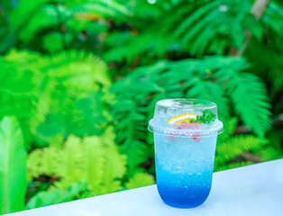 Blue Hawaii Punch drink mixed with soda water and yellow lemon placed on a table behind the green trees look natural.