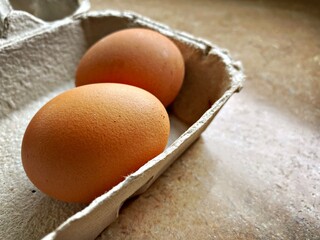 Closeup view of free range organic farm eggs in a traditional recyclable cardboard carton. Egg box details. Two eggs in a tray on the kitchen counter.