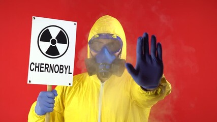 Wall Mural - Man in Protective Chemical Suit and Mask with the words CHERNOBYL. Shows Hand Stop Sign On Red Background. Smoke Around Man. Isolate, Studio.