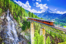 Zermatt, Switzerland. Gornergrat Tourist Train With Waterfall, Bridge And Matterhorn. Valais Region.