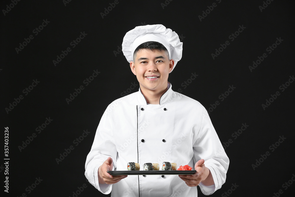 Handsome Asian chef with sushi rolls on dark background