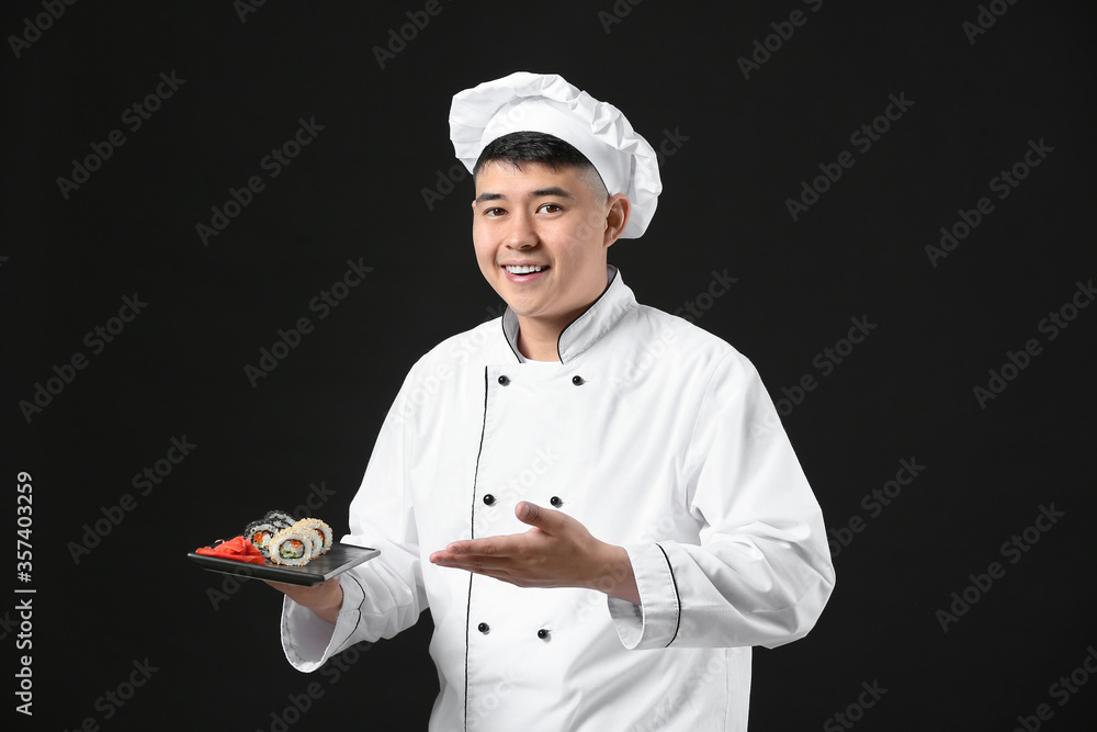 Handsome Asian chef with sushi rolls on dark background