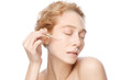 © Damir Khabirov - Young woman with blond hair applying serum to her face, looking at camera, isolated on white background. Beautiful model girl with perfect clean fresh skin.Treatment or cosmetic ads concept