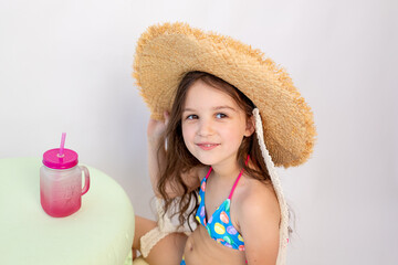 a little girl of 5-6 years old is sitting in a swimsuit with a cocktail on a white isolated background, a place for text