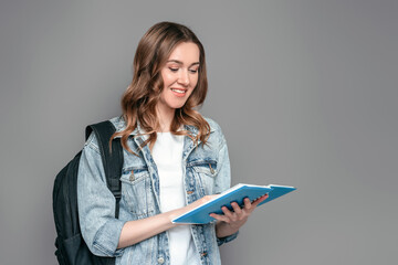 Student girl holding a notebook with homework in her hands reading and smiling isolated over grey wall background, education, distance learning, courses, exams, learning English