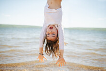 Little Hiperemotional School Age Girl Hanging Upside Down. On A Lake Shoreside.