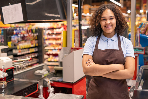 Fotografía Young smiling shop assistant or cashier in workwear crossing arms by chest
