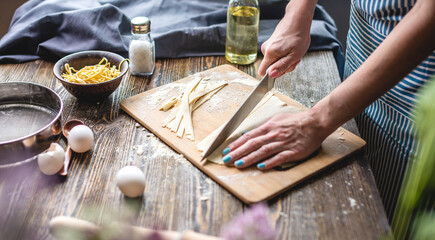 Woman is cutting raw dough with a knife to make homemade noodles. Concept of process of cooking handmade pasta