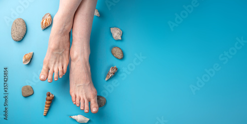 Fotografía Beautiful women's feet with beige nail polish on a blue background with seashells
