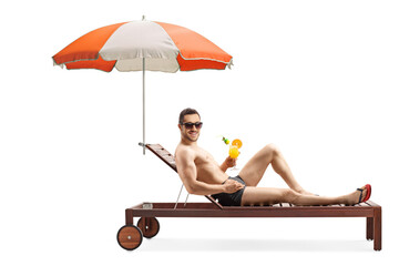 Wall Mural - Attractive young man sunbathing under umbrella and holding a cocktail