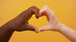 black and white hands forming heart shape together isolated on the orange background. Close up.