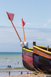 Close-Up View of Bow Section of Two Small Brightly Coloured Fishing Boats on a Stony Beach.  View of the Ocean in the distance and People on  the Shore