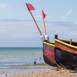 Close-Up View of Bow Section of Two Small Brightly Coloured Fishing Boats on a Stony Beach.  View of the Ocean in the distance and People on  the Shore