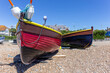 Two Brightly Coloured Fishing boats on a Stony Beach With Buildings in the Background.  Blue Sky.