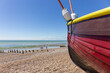 Close-Up View of Bow Section of Small Brightly coloured fishing Boat on a Stony Beach.  View of the Ocean im the distance and People Walking along the Shore