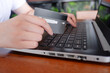 © suraphop - Cropped shot view of woman or man hands holding credit card, typing on laptop computer keyboard for internet banking and payment with phone. Online shopping.