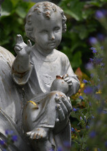 A Statue Of A Child Held By Jesus Amongst Wild Flowers