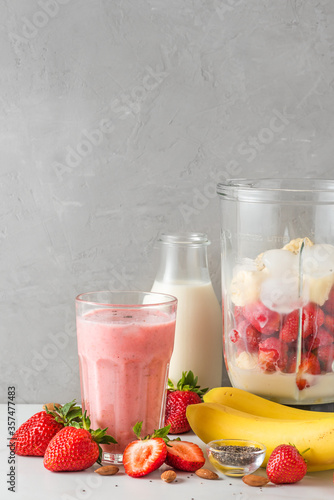 Glass of strawberry and banana vegan smoothie or milkshake made of almond milk with ingredients in blender