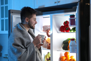 Canvas Print - Young man with cup of drink near open refrigerator at night