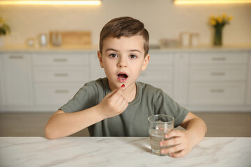 Sticker - Little boy with glass of water taking vitamin capsule in kitchen