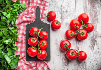 Wall Mural - Tomatoes overhead colorful arrangement on old black cutting board with kitchen cloth and parsley green leaves on wooden table studio shot