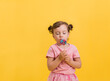 © Яна Айбазова - A little girl looks at a Lollipop on a stick on a yellow isolated background with space for text