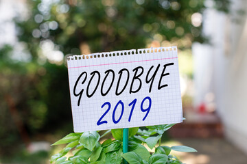 Wall Mural - Text sign showing Goodbye 2019. Business photo showcasing welcoming and celebrating a happy new year and hello 2020 Plain empty paper attached to a stick and placed in the green leafy plants