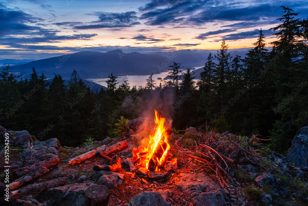 Warm Camp Fire on top of a mountain with Beautiful Canadian Nature Landscape in background during a colorful Sunset. Taken on Bowen Island, near Vancouver, British Columbia, Canada. - obrazy, fototapety, plakaty 