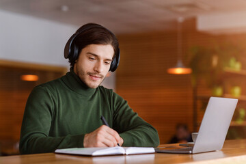 Wall Mural - Concentrated guy with headset studying online, using laptop