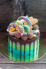 Wall Mural - Bright birthday green and blue colored cake decorated with chocolate, cake pops, lollipop, waffle and cupcake.