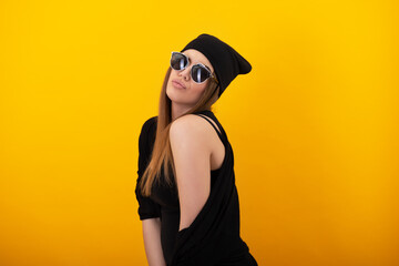 Leinwandbilder - Stylish girl with sunglasses over yellow background. Studio female portrait. Happy charming woman wearing black clothes posing indoor