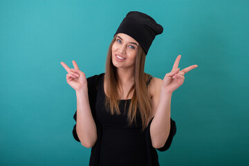 Leinwandbilder - Attractive girl with winner gesture over turquoise background. Studio female portrait. Young happy smiling woman makes victory sign with her hands