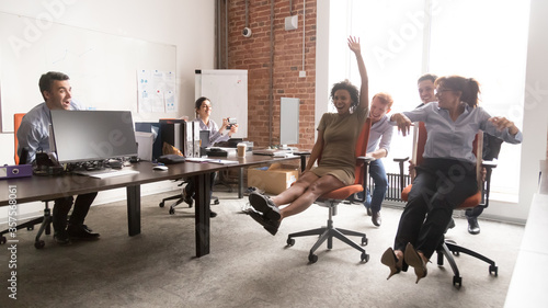 Fotografía Happy diverse colleagues having fun together, riding in office chair, excited em