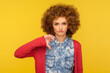 I don't like this! Portrait of upset woman with curly hair in casual outfit standing with thumbs down gesture, expressing disapproval, criticizing bad service. indoor studio shot, yellow background