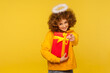 © khosrork - Hey you, happy holidays! Portrait of cheerful curly-haired angelic woman with saint nimbus pointing to camera and holding wrapped christmas gift box. indoor studio shot isolated on yellow background