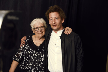 Wall Mural - Two generations. Indoor family portrait of mature wrinkled gray haired woman dressed in stylish blouse, surrounded with love of son, enjoying time together, isolated on black studio wall. Film effect.