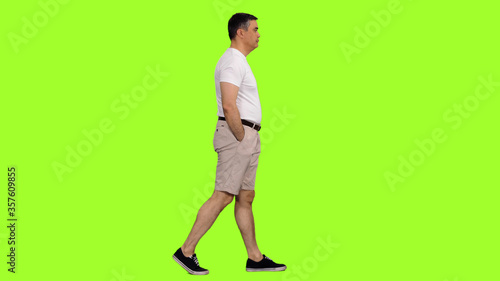 Cuadros en Lienzo Side view of a man in shorts and white t-shirt walking on green screen backgroun