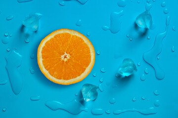 fresh juicy slice of orange and ice cubes on the bright blue background covered with water drops.