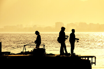 Poster - Silhouetted people relaxing and fishing on Antalya harbor over yellow colored dusk time in Antalya, Turkey