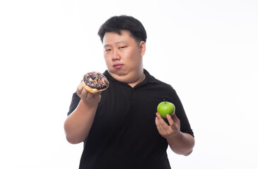 Young Funny Fat Asian man choosing between chocolate donuts and green apple isolated on white background, Healthy lifestyle concept.