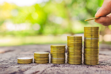 investor business man hand putting money on coins row stack on wood table with blur nature park background. money saving concept for financial banking and accounting.