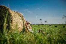 Beautiful Girl Is Resting After Work. Girl On The Field With Hay. Woman Near A Sheaf Of Hay In A Field. Rural Life. Holidays In The Village