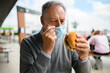 © Minerva Studio - Mature man trying to eat a hamburger wearing a mask, funny coronavirus concept