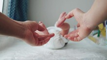 Little Legs Of A Newborn Baby. The Child Moves His Legs. Defocus. New Life. Baby In The Diaper. Father Catches The Child Legs With His Hands On Swaddling Table Indoors