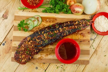 Poster - Long piece of meat with seasonings served on a wooden tray with a small bowl of sauce