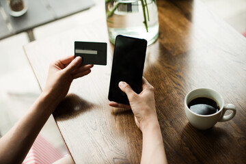 Online payment. Woman 's hands holding a credit card and using smart phone for online shopping or for paying for coffee in cafe. Indoor close-up. Online shopping concept