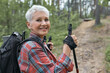 © Anatoliy Karlyuk - Active lifestyle, aging, travel and hiking concept. Outdoor image of beautiful energetic mature woman with backpack using poles, enjoying nordic walking in forest, looking at camera with happy smile